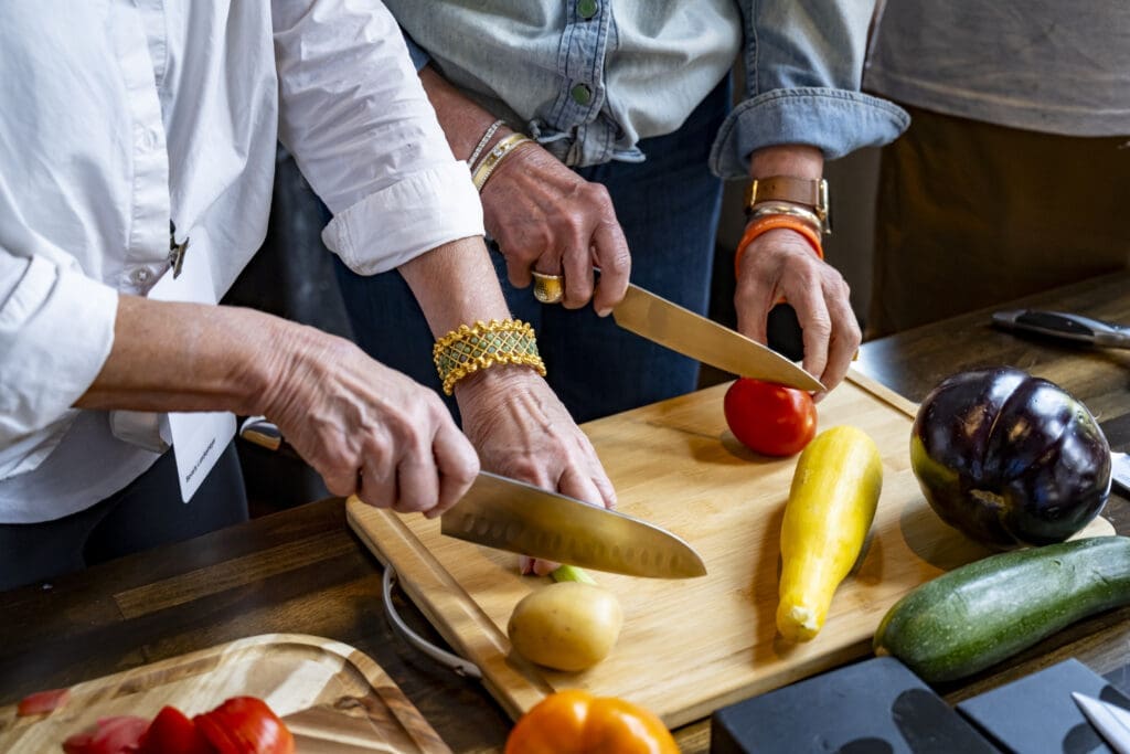Two pairs of hands cutting vegetables